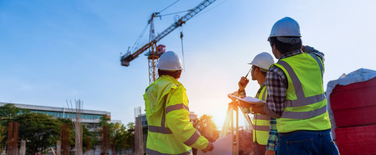 diskutierende Bauarbeiter vor einen Morgenhimmel mmit Kran